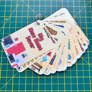 May include: A set of cards with illustrations of home decor items and the text "My New Home Saver" and "Sparkle Designs" on the front. The cards are fanned out and held together with a ring. The text "£20" is visible on two of the cards.