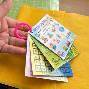 May include: A colourful game board with a pink ring attached. The game board has a grid with numbers and pound signs. The game board is titled "Fill the toy box".