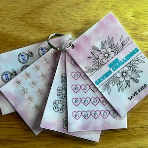 May include: A set of six pink and white cards with a floral design and the text "MINI SAVING CHALLENGES" and "SAVE £250". Each card has a different design of coins, stars, or hearts with the amount to save on each.