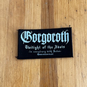 May include: Black rectangular patch featuring the word "Gorgoroth" in white gothic lettering. Beneath, the text reads "Twilight of the Idols -in conspiracy with Satan- ©2002 NUCLEAR BLAST". The patch is on a wooden surface.