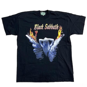 May include: Black t-shirt featuring the band name "Black Sabbath" in gold lettering above a graphic of a figure with blue wings and flames. The graphic is centered on the front of the shirt.