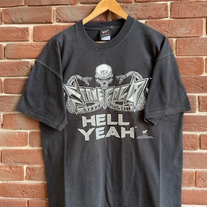 Puede incluir: Camiseta negra con un diseño gráfico que incluye el texto "STONE COLD" y "HELL YEAH". El diseño incluye una calavera, estrellas y el nombre "STEVE AUSTIN". La camiseta tiene mangas cortas y cuello redondo.