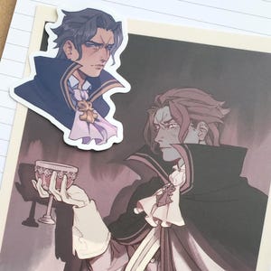May include: An illustration of a character in a dark coat and white shirt, holding a goblet. A sticker of the same character is placed above the illustration. The artwork has a gothic or fantasy theme, with a color palette of black, white, and shades of purple.