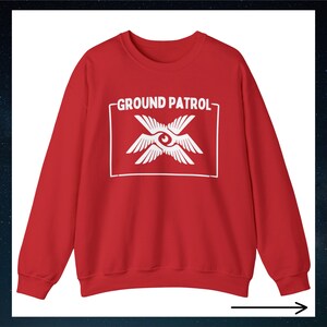 May include: Red sweatshirt with a white graphic of a stylized eye with wings and the text "GROUND PATROL" in a white rectangle.