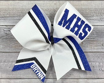 May include: White cheerleading bow with blue and black accents. The bow features the letters "MHS" in blue glitter on one side and the name "BRYNN" on the other. The bow has a classic ribbon design.