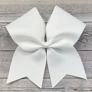 May include: A large white cheer bow with a simple design. The bow is made of a thick, textured ribbon and is tied with a single knot in the center.