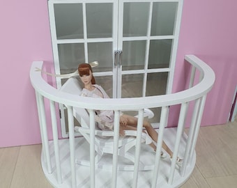 May include: White dollhouse balcony with a white rocking chair and a doll sitting in it. The balcony has a white railing and a white floor.