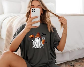 May include: A gray short-sleeved shirt with a graphic of a ghost wearing a hat and holding a pumpkin and a drink. The shirt is part of a matching set with gray shorts.