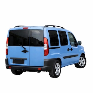 May include: A light blue passenger van featuring black roof rails, tinted rear windows, and black door handles. The vehicle has a rear wiper, vertical taillights, and silver alloy wheels. The rear bumper and side trim are finished in matte black.