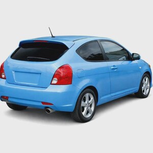 May include: A light blue hatchback car viewed from the rear three-quarter angle. The vehicle features a rear windscreen wiper, a small roof-mounted aerial, red tail lights, silver alloy wheels, and a single exhaust pipe visible on the lower left.
