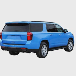 May include: A bright blue SUV shown from a rear three-quarter angle. The vehicle features a black roof rack, tinted rear windows, vertical red taillights, a black rear bumper with integrated exhaust outlets, and silver multi-spoke alloy wheels.