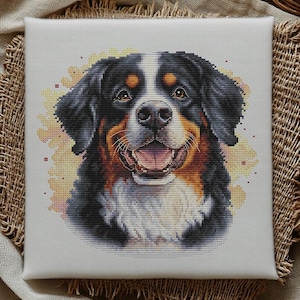 May include: A square canvas featuring a cross-stitch portrait of a Bernese Mountain Dog. The dog has black, brown, and white fur, with a happy expression. The background has yellow floral accents. The text "BananiStitchery" is at the bottom.
