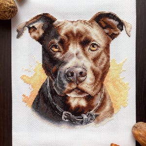 May include: Cross-stitch embroidery of a brown pit bull dog with a black collar. The dog is looking directly at the viewer with a serious expression. The background is a light yellow watercolor wash.