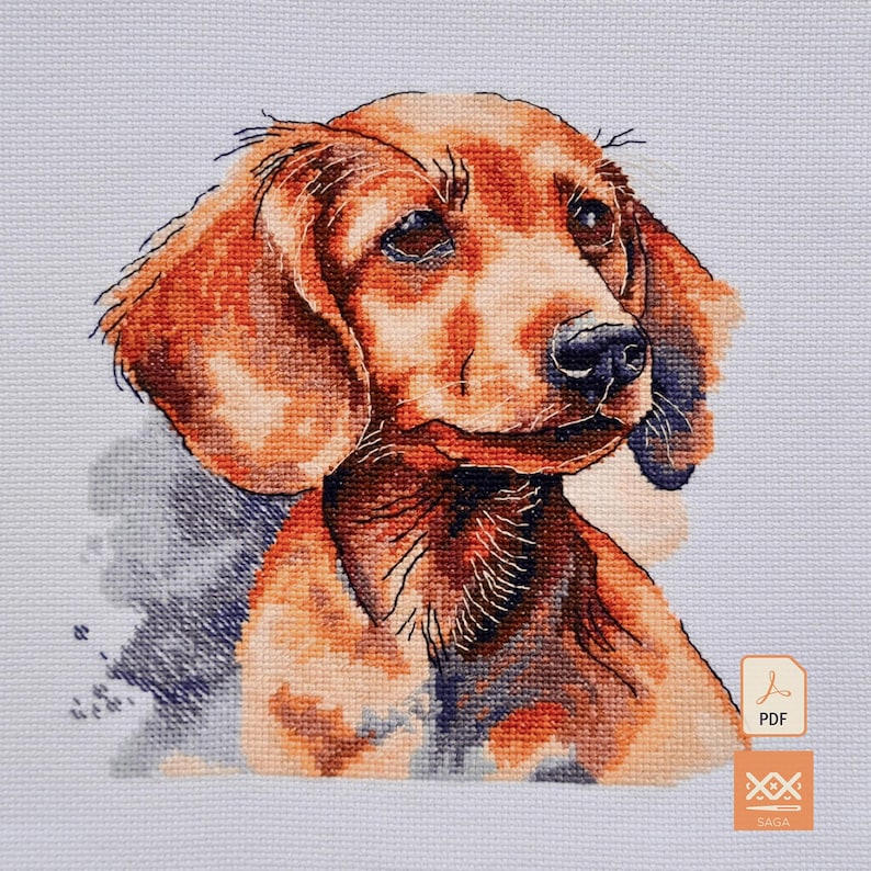 May include: A cross-stitch pattern featuring a portrait of a brown dachshund dog with floppy ears and a black nose, rendered in shades of orange, brown, and dark blue on a light blue grid fabric, with a small PDF icon in the corner.