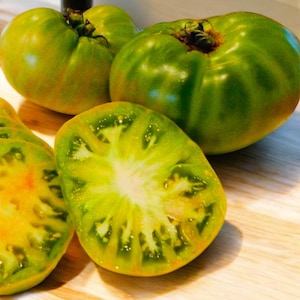 May include: Four green tomatoes, one sliced in half, showing the inside of the fruit. The tomatoes are on a wooden surface.