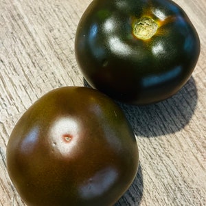 Op de afbeelding: Twee donkerpaarse heirloom tomaten met een glanzende afwerking. De tomaten zijn rond en hebben een lichte inkeping aan de bovenkant.
