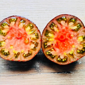 Peut inclure: Deux moitiés d'une tomate ancienne mûre, coupées pour révéler l'intérieur. La chair de la tomate est d'un rouge vif, passant au jaune et au vert près des graines. La peau est d'un rouge foncé. La tomate est sur une surface en bois.
