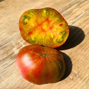 Könnte beinhalten: Eine halbierte Tomate mit dunkelgrüner Außenseite und leuchtend gelbem und rotem Inneren. Eine ganze Tomate mit dunkelgrüner Außenseite und rotem und gelbem Inneren ist ebenfalls zu sehen.