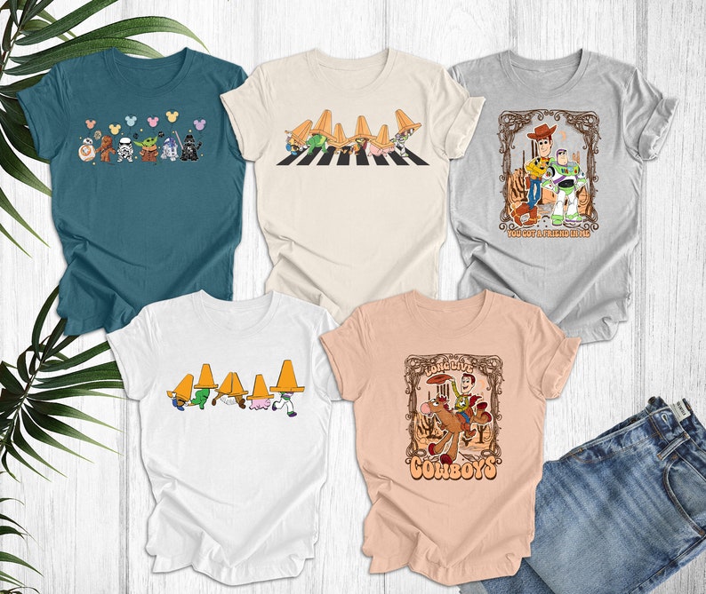 May include: Five different t-shirts with various cartoon characters and designs. The shirts are all white, light beige, light blue, and light pink. The designs include a group of cartoon characters walking across a crosswalk, a group of cartoon characters wearing sombreros, a cartoon character riding a horse, and a cartoon character with a friend.