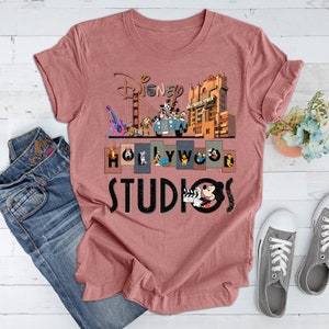 May include: A pink t-shirt with a graphic print of Disney characters in front of the Hollywood Tower Hotel and the Golden Gate Bridge. The text "Disney Hollywood Studios" is printed below the graphic.