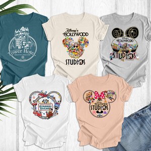 May include: Five different t-shirts featuring Disney's Hollywood Studios. The shirts are white, light blue, gray, and peach. The designs include Mickey Mouse ears, the Tower of Terror, and the Runaway Railway.