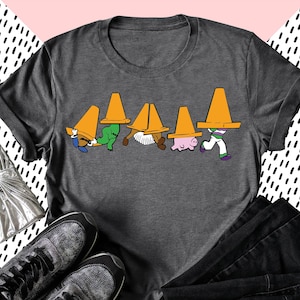 May include: A dark gray t-shirt with a graphic of Toy Story characters wearing orange traffic cones on their heads. The characters include Woody, Buzz Lightyear, Jessie, Hamm, and Rex.