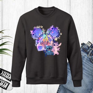 Puede incluir: Sudadera negra de cuello redondo con un gr&aacute;fico colorido de un castillo, Stitch y Angel. El dise&ntilde;o est&aacute; dentro de una forma de cabeza de Mickey Mouse. La sudadera se combina con vaqueros azules y zapatillas deportivas blancas y negras.