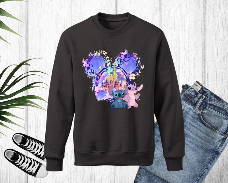 Puede incluir: Sudadera negra de cuello redondo con un gr&aacute;fico colorido de un castillo, Stitch y Angel. El dise&ntilde;o est&aacute; dentro de una forma de cabeza de Mickey Mouse. La sudadera se combina con vaqueros azules y zapatillas deportivas blancas y negras.