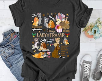 May include: A dark gray t-shirt with a graphic print of Lady and the Tramp characters. The print includes the text "Start Building Some Memories", "Disney", "Lady and the Tramp", "Lady", "The Tramp", "Bella Notte", "Est. 1955", and "Everybody Knows a Dog's Best Friend is His Human".