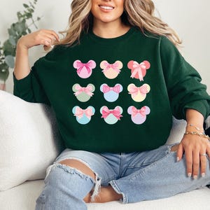 Puede incluir: Una sudadera verde oscuro con un patr&oacute;n de nueve dise&ntilde;os coloridos en forma de lazo. Cada lazo es de un color pastel diferente, con acentos rosas, azules y amarillos. La sudadera es de estilo casual, adecuada para el uso diario.