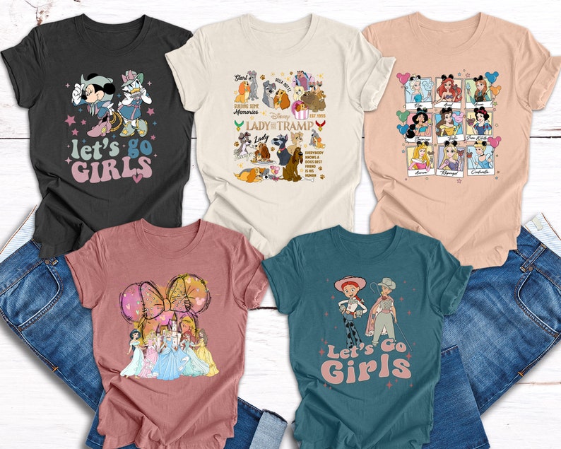 May include: Five different t-shirts featuring various Disney characters. The shirts are in a variety of colours and all have the text "Let's Go Girls" printed on them.