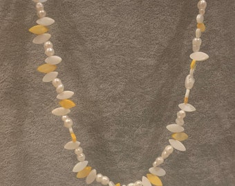 May include: A white and yellow shell necklace with a leaf design. The necklace is made of small, round pearls and oval-shaped shells.