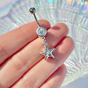 May include: A silver belly button ring with a clear crystal and a dangling star charm.