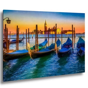 May include: A vibrant canvas print depicts gondolas docked in Venice at sunset. The water reflects the warm hues of the sky, with the city's architecture silhouetted in the background. The gondolas are black with blue covers.
