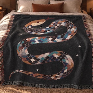 May include: A black woven throw blanket featuring a large, multi-colored snake graphic with a diamond-patterned scale design. The snake is depicted in shades of blue, orange, and white, accented by small white cross symbols. The blanket has fringed edges.