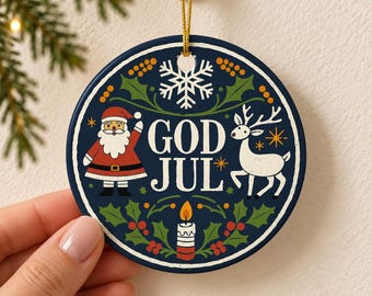 Puede incluir: Un adorno navideño redondo de cerámica azul oscuro con el texto blanco GOD JUL en el centro. El diseño incluye un Santa Claus con traje rojo, un reno blanco, un copo de nieve blanco, una vela encendida y hojas de acebo verdes con bayas rojas.