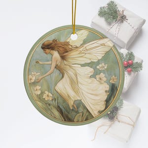 May include: A round ceramic ornament featuring a vintage illustration of a fairy with wings, wearing a white dress and flying over green foliage with white flowers.