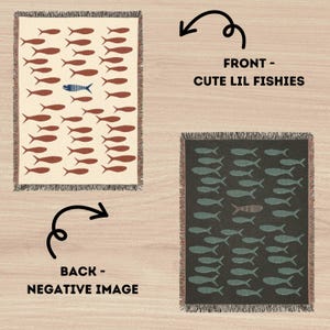 May include: A reversible throw blanket with a fish pattern. The front side features brown fish on a cream background, with one blue fish. The back side has a negative image with teal fish on a dark background. The text reads "FRONT - CUTE LIL FISHIES" and "BACK - NEGATIVE IMAGE".