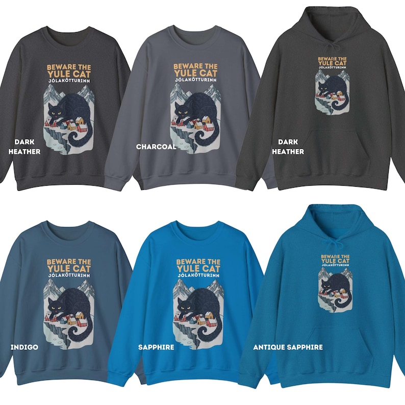May include: A collection of six sweatshirts and hoodies in dark heather, charcoal, indigo, sapphire, and antique sapphire colors. Each garment features a graphic of a black cat over a snowy mountain village with the text BEWARE THE YULE CAT J&Oacute;LAK&Ouml;TTURINN.