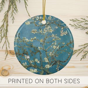 Könnte beinhalten: Runder Keramikschmuck mit einem Gemälde eines blühenden Mandelbaums vor einem tealblauen Hintergrund. Das Kunstwerk zeigt weiße Blüten und braune Äste. Der Schmuck hat eine goldene Schnur zum Aufhängen und den Text "PRINTED ON BOTH SIDES".