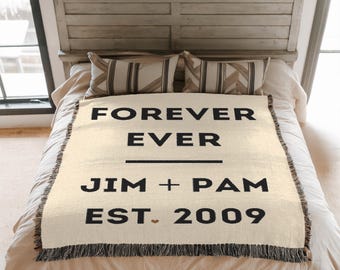 May include: Cream-colored woven throw blanket with black text that reads "FOREVER EVER" above "JIM + PAM EST. 2009". The blanket has a fringed edge and is displayed on a bed with pillows.