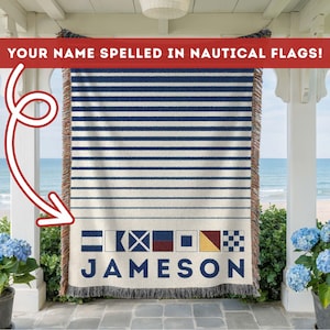 May include: A woven throw blanket with a nautical theme. The blanket features horizontal navy blue stripes on a cream background. The name "JAMESON" is spelled out in nautical flags at the bottom. The text "YOUR NAME SPELLED IN NAUTICAL FLAGS!" is at the top.