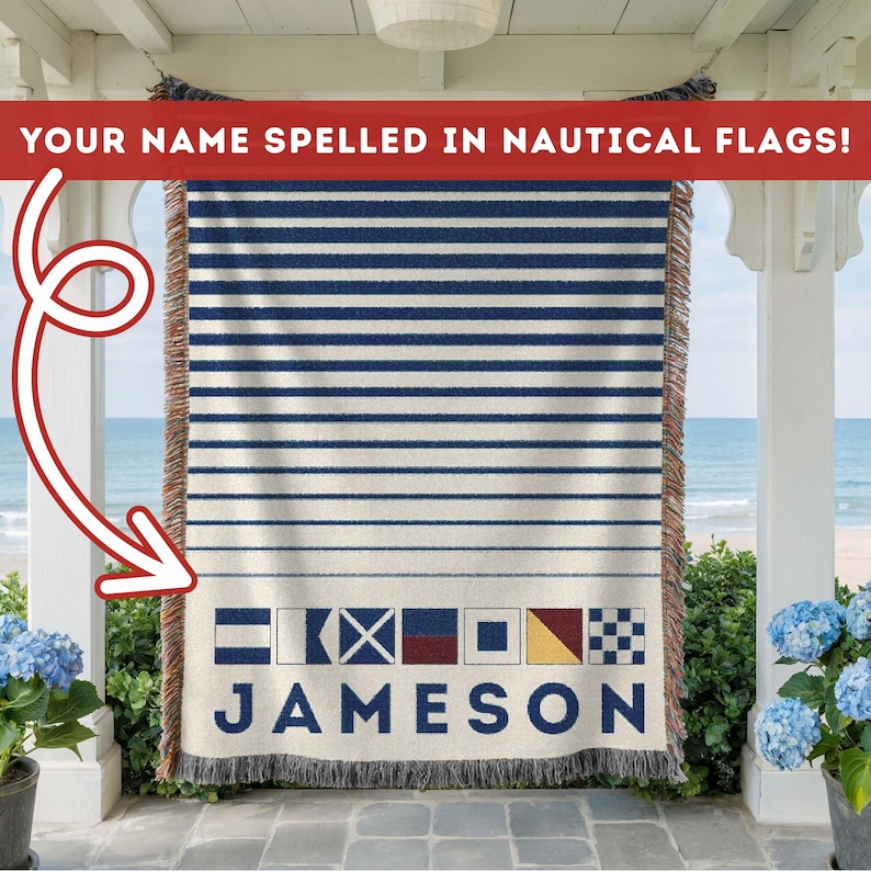 May include: A woven throw blanket with a nautical theme. The blanket features horizontal navy blue stripes on a cream background. The name "JAMESON" is spelled out in nautical flags at the bottom. The text "YOUR NAME SPELLED IN NAUTICAL FLAGS!" is at the top.