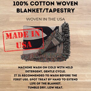 May include: A 100% cotton woven blanket or tapestry with fringed edges. The text reads 100% COTTON WOVEN BLANKET/TAPESTRY, WOVEN IN THE USA, MADE IN USA, and includes care instructions: MACHINE WASH ON COLD WITH MILD DETERGENT, GENTLE CYCLE.