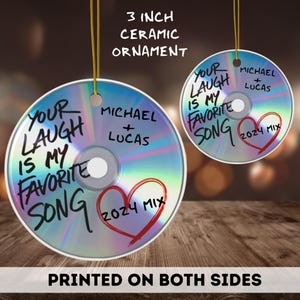 May include: A 3 inch ceramic ornament shaped like a CD with a holographic finish. The ornament has a heart with the text "2024 Mix" and the text "Your laugh is my favorite song" written on it. The ornament also has the text "Michael + Lucas" written on it.