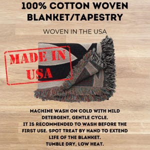 May include: A folded black and beige woven blanket with fringe. The blanket has a geometric design and the text "100% COTTON WOVEN BLANKET/TAPESTRY" is at the top. The blanket is stamped with "MADE IN USA".