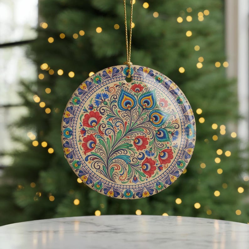 May include: A round, decorative ornament with a floral design. The ornament features a cream-colored background with a colorful pattern of red, blue, and green flowers and leaves. A gold string is attached for hanging. The ornament is likely for the holidays.