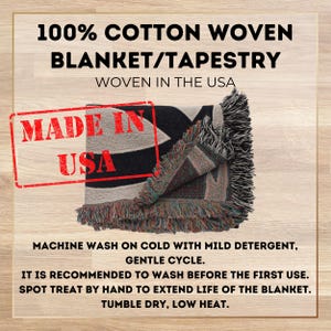 May include: A black and white woven tapestry blanket with fringe. The blanket is folded in half and has the words "Made in USA" printed on it. The text "100% Cotton Woven Blanket/Tapestry Woven in the USA" is printed above the blanket. The text below the blanket reads "Machine wash on cold with mild detergent, gentle cycle. It is recommended to wash before the first use. Spot treat by hand to extend life of the blanket. Tumble dry, low heat."