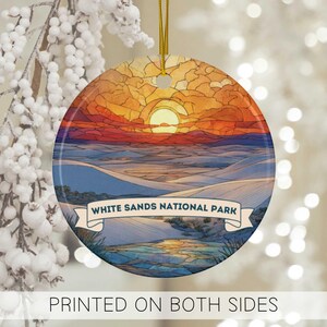 May include: Round ceramic ornament featuring a sunset over White Sands National Park. The design includes a banner with the park's name and a gold hanging cord. The text "PRINTED ON BOTH SIDES" is at the bottom.