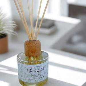 May include: A glass reed diffuser with a wooden top and reeds. The label reads "The Bridgefield Candle Company" with a botanical design. The diffuser contains 100ml of liquid and is on a white surface.